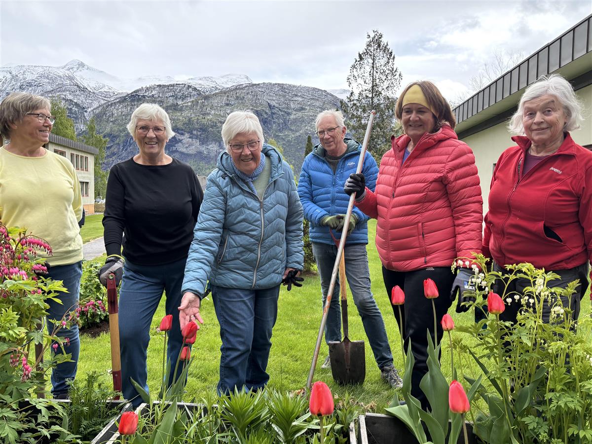 Blide personar smilar mot kamer attmed blomsterbed - Klikk for stort bilete